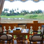 A small wooden table and chairs on a boat deck overlooking a lush Nile riverbank.