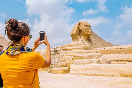 A tourist taking a photo of the Great Sphinx of Giza during a luxury Cairo Nile cruise Hurghada 12 days tour package.