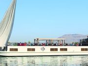 Profile view of the Merit Star Dahabiya sailing on the Nile with desert mountains in the background.