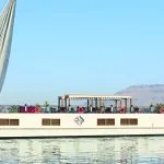 Profile view of the Merit Star Dahabiya sailing on the Nile with desert mountains in the background.