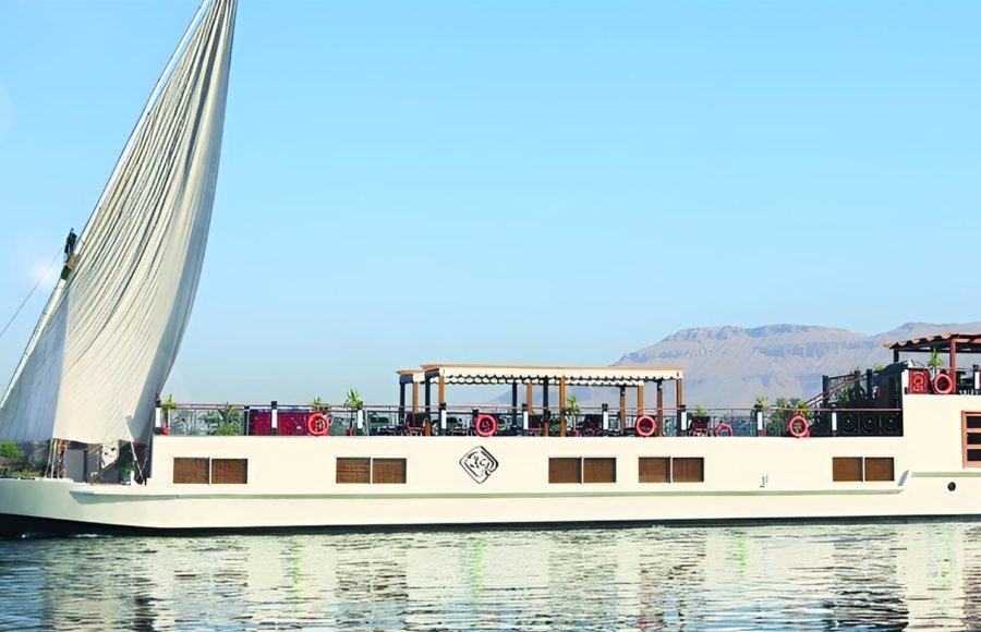 Profile view of the Merit Star Dahabiya sailing on the Nile with desert mountains in the background.