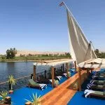 Wide view of the blue-carpeted sundeck of the Merit Star Dahabiya with a large white sail against a desert landscape.