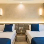 Modern twin bedroom on a Dahabiya with two beds, blue pillows, and warm wall lighting.