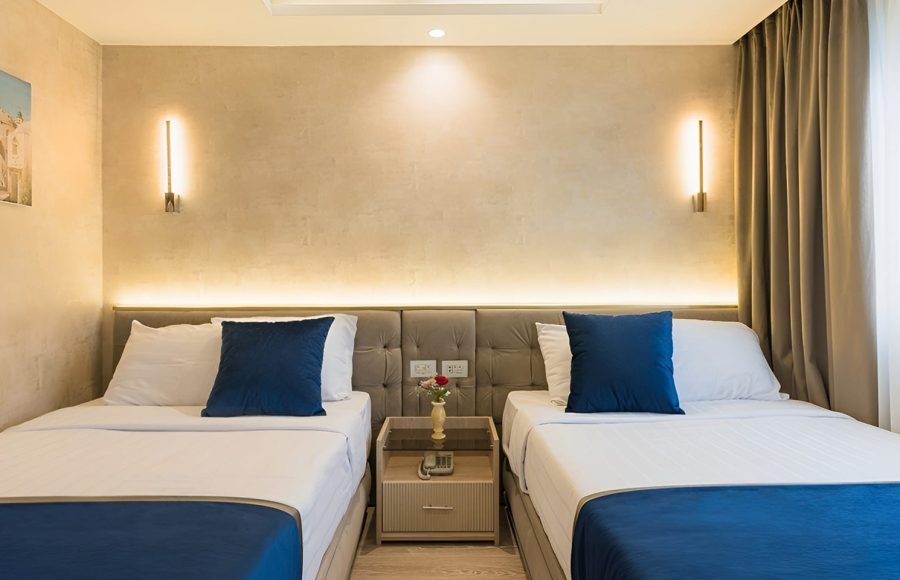 Modern twin bedroom on a Dahabiya with two beds, blue pillows, and warm wall lighting.