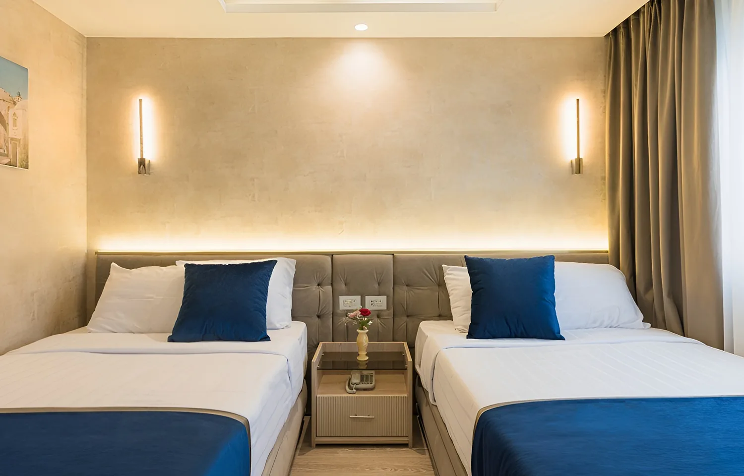 Modern twin bedroom on a Dahabiya with two beds, blue pillows, and warm wall lighting.