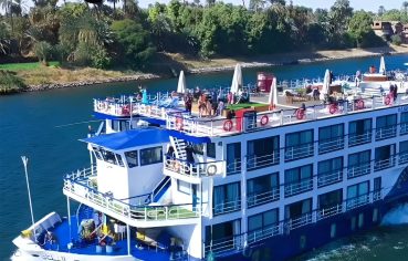 Exterior side view of the MS Al Nabilatan Nile Cruise ship sailing past lush riverbanks.