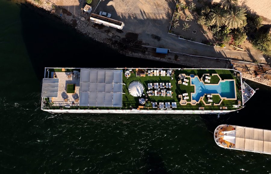 An Aerial View of the sun deck of the MS Alma Nile Cruise, showcasing the swimming pool, lounge chairs, and shaded seating areas while docked on the Nile River.