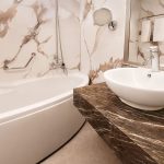 A modern, elegant bathroom aboard the MS Alma Nile Cruise, featuring marble wall panels, a sleek bathtub, and a dark marble vanity with a contemporary vessel sink.