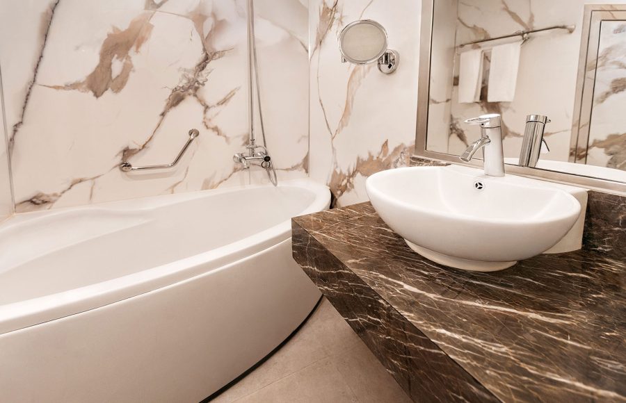 A modern, elegant bathroom aboard the MS Alma Nile Cruise, featuring marble wall panels, a sleek bathtub, and a dark marble vanity with a contemporary vessel sink.