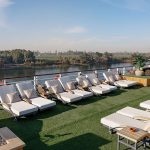 Comfortable lounge chairs and sunbeds lined up on the lush Sun Deck of the MS Alma Nile Cruise, offering panoramic views of the Nile River and green riverbanks.
