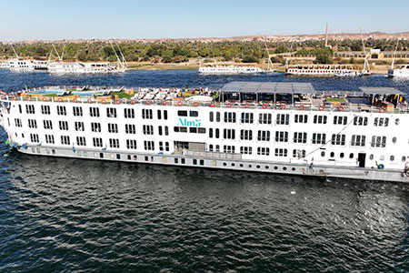 The white deluxe MS Alma Nile Cruise sailing along the Nile River, featuring an expansive sundeck with a swimming pool and panoramic views of the verdant Egyptian riverbank.