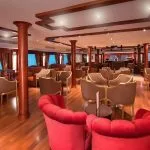 Upscale ship lounge with red velvet chairs and wood accents.