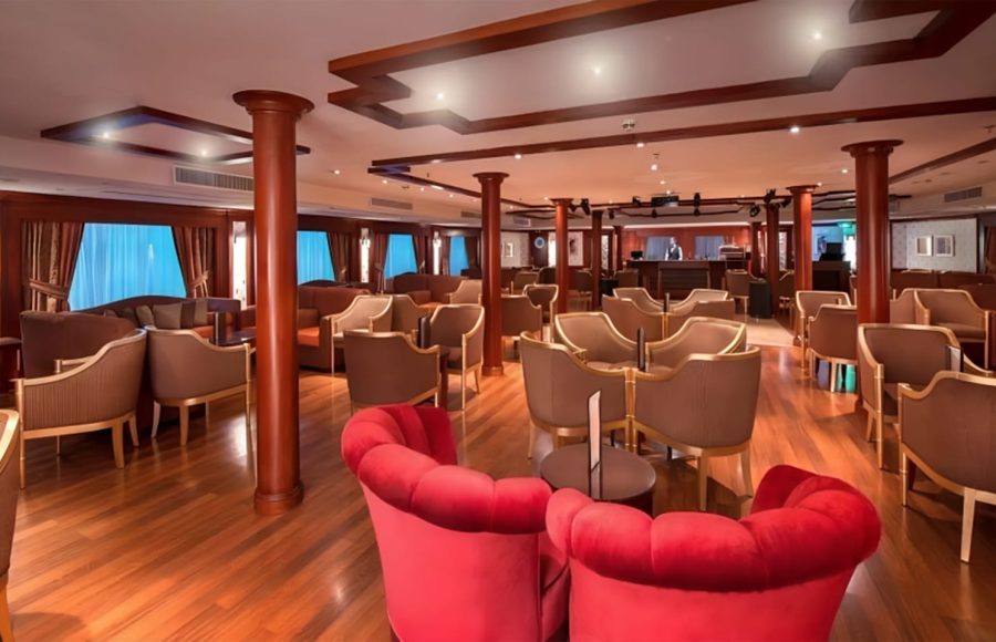 Upscale ship lounge with red velvet chairs and wood accents.