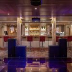 A stylish bar and lounge area aboard the MS Chateau Lafayette Nile Cruise, featuring ambient purple lighting, modern bar stools, and a well-stocked counter.