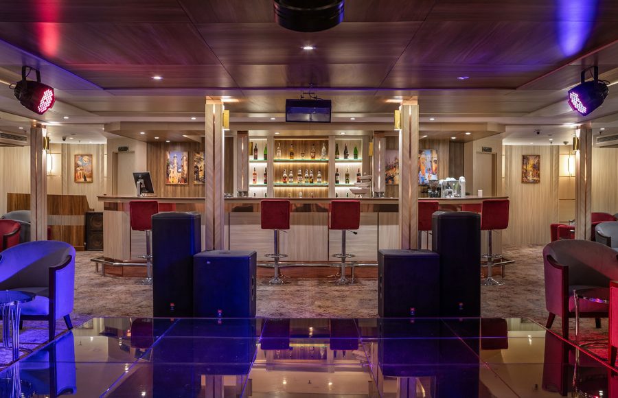 A stylish bar and lounge area aboard the MS Chateau Lafayette Nile Cruise, featuring ambient purple lighting, modern bar stools, and a well-stocked counter.