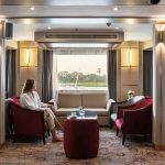 A guest relaxing in the elegant restaurant lounge on the MS Chateau Lafayette Nile Cruise, featuring stylish seating and large panoramic windows overlooking the riverbanks.