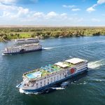 Aerial view of the MS Chateau Lafayette Nile Cruise sailing along the scenic Nile River with other vessels in the background under a bright blue sky.