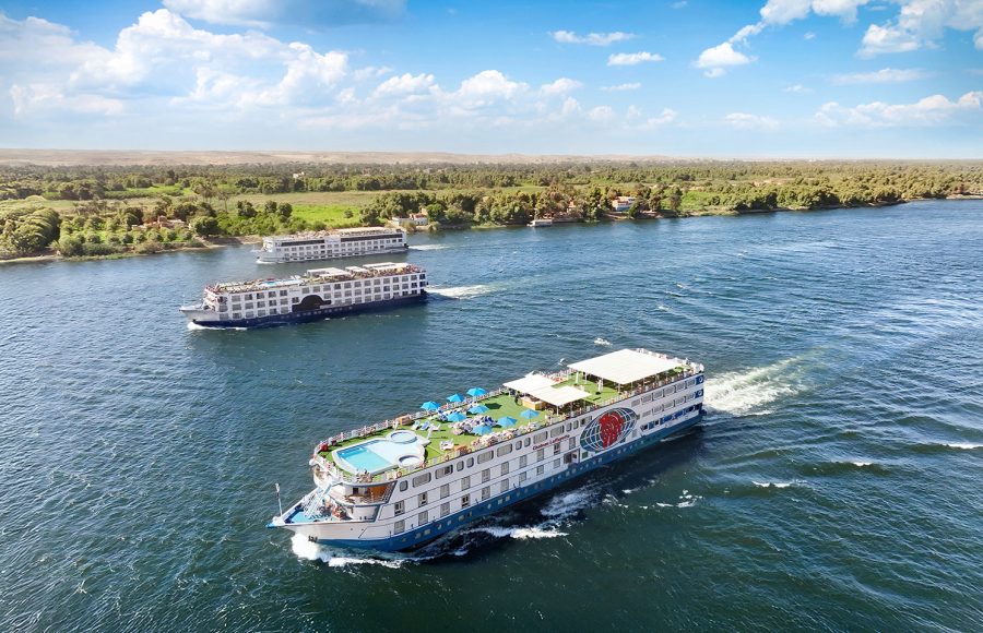 Aerial view of the MS Chateau Lafayette Nile Cruise sailing along the scenic Nile River with other vessels in the background under a bright blue sky.