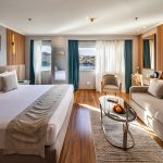 A spacious and luxurious suite aboard the MS Chateau Lafayette Nile Cruise, featuring a plush king-size bed, a comfortable sitting area, and large windows with river views.