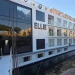 The MS Ellie Nile Cruise ship docked at night, brightly lit with exterior lighting against a dark sky and reflected on the boardwalk.
