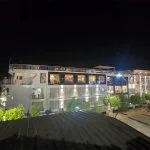 The MS Ellie Nile Cruise ship docked at night, brightly lit with exterior lighting against a dark sky and reflected on the boardwalk.