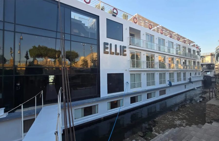 The MS Ellie Nile Cruise ship docked at night, brightly lit with exterior lighting against a dark sky and reflected on the boardwalk.