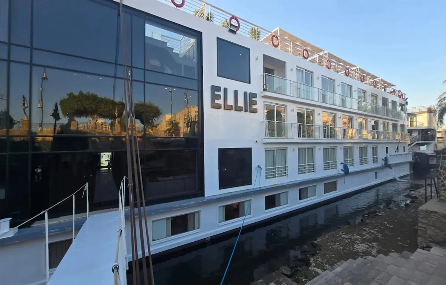 The MS Ellie Nile Cruise ship docked at night, brightly lit with exterior lighting against a dark sky and reflected on the boardwalk.