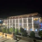 The MS Ellie Nile Cruise ship docked at night, brightly lit with exterior lighting against a dark sky and reflected on the boardwalk.