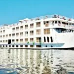 Exterior view of the MS Ellie Nile Cruise ship, a multi-deck white vessel sailing on the Nile River under a clear blue sky.