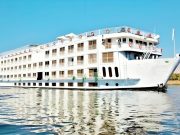 Exterior view of the MS Ellie Nile Cruise ship, a multi-deck white vessel sailing on the Nile River under a clear blue sky.