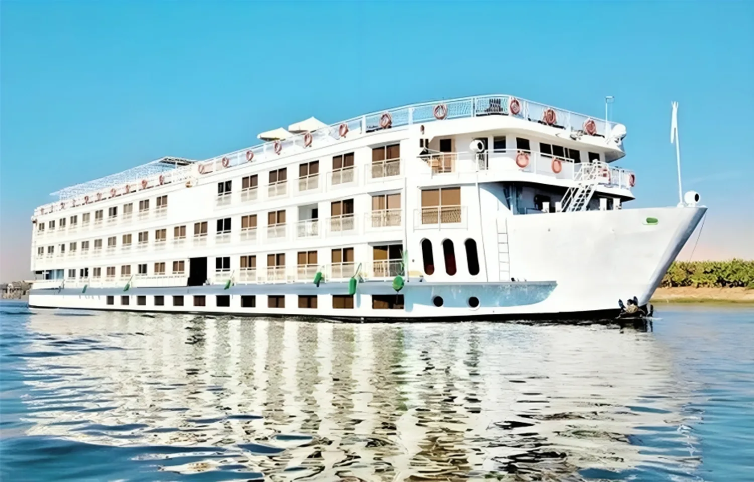 Exterior view of the MS Ellie Nile Cruise ship, a multi-deck white vessel sailing on the Nile River under a clear blue sky.