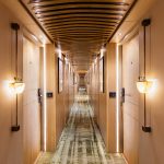 A modern and elegantly lit corridor on the MS Esmeralda Nile Cruise, featuring warm wood paneling, stylish wall sconces, and patterned carpeting leading down the ship's hallway.