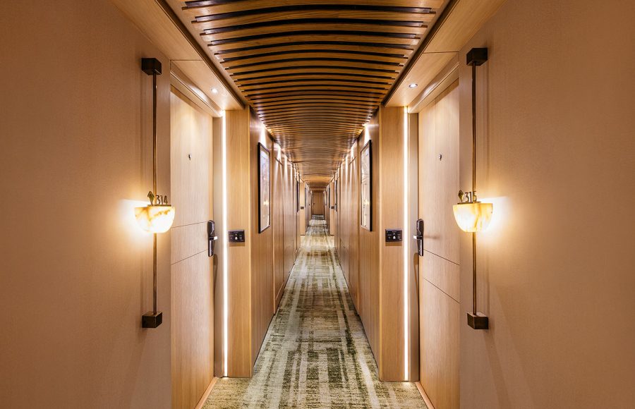 A modern and elegantly lit corridor on the MS Esmeralda Nile Cruise, featuring warm wood paneling, stylish wall sconces, and patterned carpeting leading down the ship's hallway.