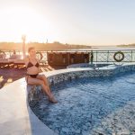 A guest relaxing by the outdoor Swimming Pool on the MS Esmeralda Nile Cruise, enjoying a refreshing drink with scenic views of the Nile River at sunset.