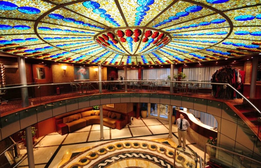 Ship's multi-level atrium with a colorful, circular stained-glass ceiling and main reception desk.