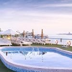 The sun deck of the MS Hapi Nile cruise ship featuring a small outdoor swimming pool. The deck is covered in green artificial turf and lined with white lounge chairs and sun umbrellas overlooking the river.