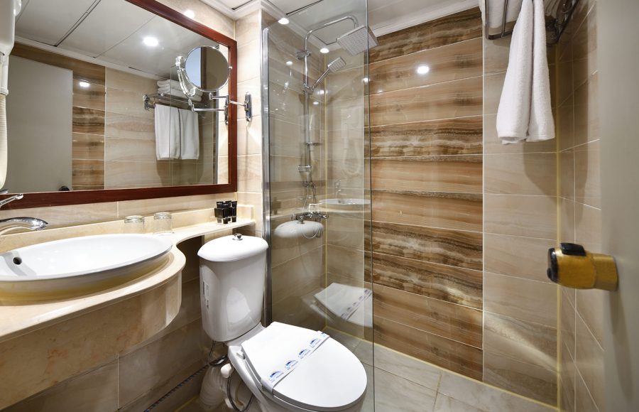 A modern and clean bathroom aboard the MS Nile Treasure Cruise, featuring a glass-enclosed walk-in shower, a stylish vanity sink, and warm marble-toned tiling.