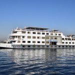 The MS Nile Treasure Cruise ship sailing smoothly along the picturesque waters of the Nile River under a clear blue sky.