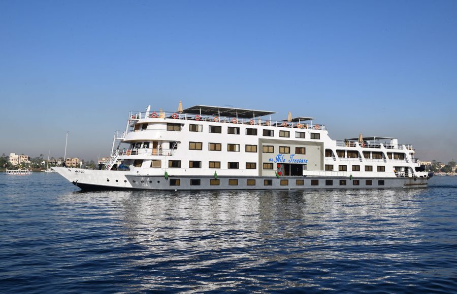 The MS Nile Treasure Cruise ship sailing smoothly along the picturesque waters of the Nile River under a clear blue sky.