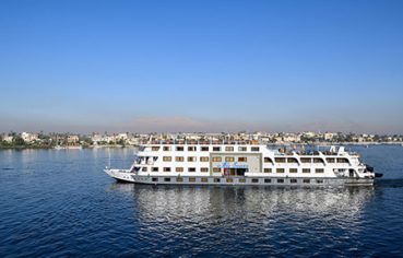 Exterior side view of the MS Nile Treasure Cruise vessel sailing smoothly along the open waters of the Nile River under a clear blue sky.