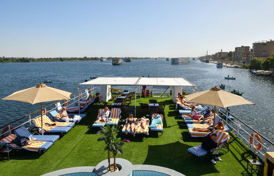 Guests relaxing on the sun deck of the MS Nile Treasure Cruise, featuring lounge chairs, sun umbrellas, and panoramic views of the Nile River.