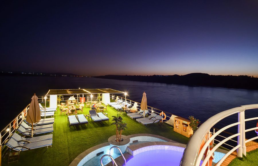 The illuminated sun deck at sunset on the MS Nile Treasure Cruise, featuring lounge chairs, an outdoor pool, and a breathtaking view of the Nile River at dusk.