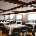 Elegant dining room on the MS Nile Plaza cruise ship with set tables, dark gray chairs, and a dark wood coffered ceiling.