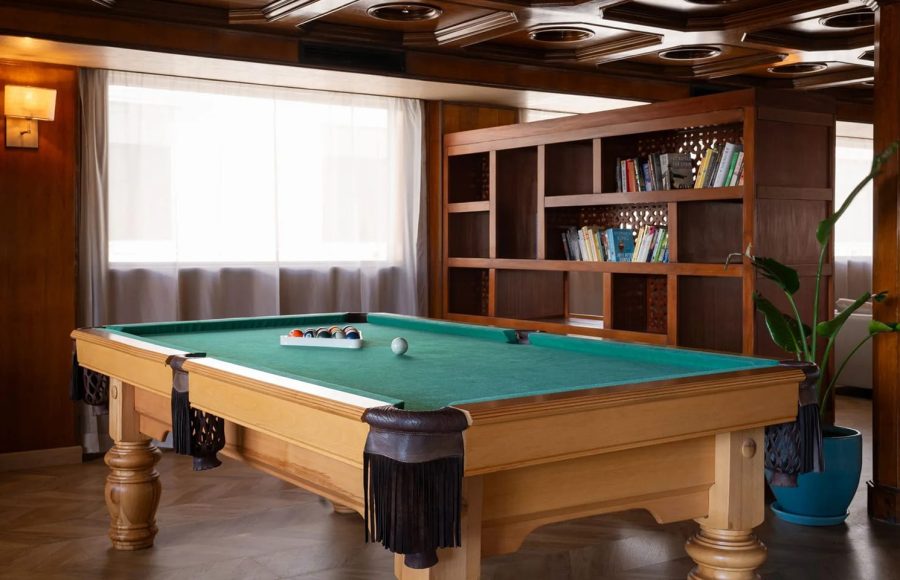 Billiards room on the MS Nile Plaza featuring a light wood pool table with a green felt, a coffered wood ceiling, and a large wooden bookshelf.