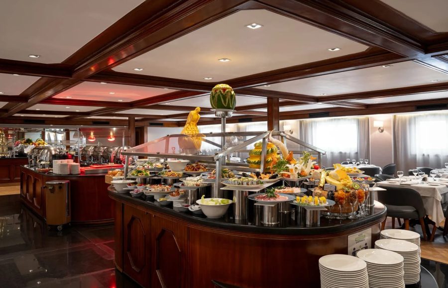 Close-up of the elaborate, central buffet island on the MS Nile Plaza, laden with colorful food, platters, and a decorative melon carving.