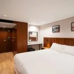 View of a modern Nile cruise ship cabin with a king-sized bed, dark wood wardrobe and doors, a small vanity, and two pieces of framed artwork.