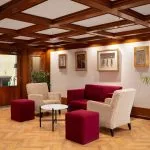 Cozy lounge area on the MS Nile Plaza with beige armchairs, red ottomans, and a coffered wood ceiling, featuring Egyptian-themed artwork.