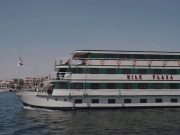 MS Nile Plaza cruise ship sailing on the Nile River under a clear blue sky, showing its white and green exterior.