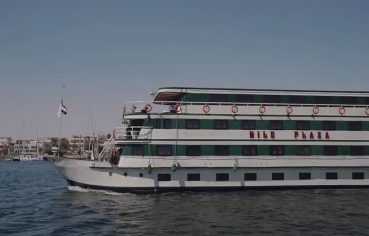 MS Nile Plaza cruise ship sailing on the Nile River under a clear blue sky, showing its white and green exterior.