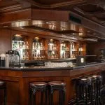 Angled view of the elegant MS Nile Plaza bar, showing the rich, polished wood counter, tiered bottle display, and brown leather bar stools.